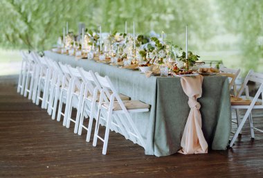 Yeşilliğin ve sakin atmosferin ortasında bir kutlama için hazırlanmış zarif ve uzun bir yemek masası..