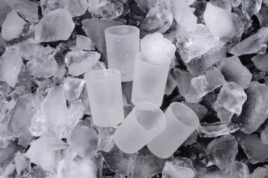 Frosted shot glasses are resting on a bed of crushed ice, perfect for a refreshing drink. Ideal for cocktails or shots in a winter gathering. clipart