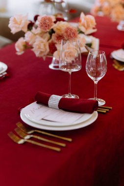 Zengin bir bordo masa örtüsü, zarif bir bulaşık takımı ve çarpıcı bir çiçek süsü içeren güzel düzenlenmiş bir yemek masası, lüks yemek etkinlikleri için mükemmel..