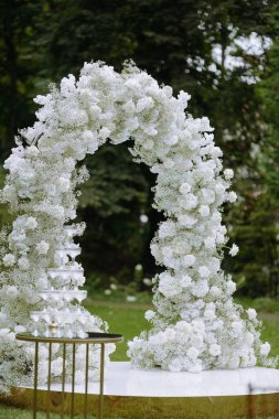 Beyaz güller ve çingenelerle süslenmiş güzel düzenlenmiş bir çiçek kemeri, bereketli bir açık hava ortamında serin bir atmosfer yaratır..