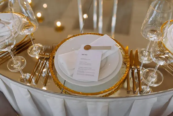 Güzel düzenlenmiş bir menü kartı, ince cam eşyalar ve parıldayan çatal bıçaklar içeren zarif bir masa. Düğünler ve üst düzey etkinlikler için mükemmel..