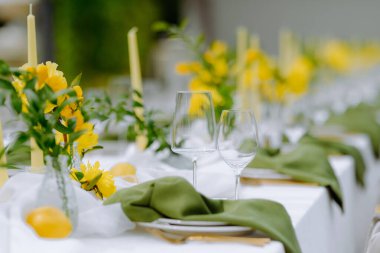 Sarı çiçekli güzel bir yemek masası, yeşil peçeteler, ve şık cam eşyalar, etkinlikler ve kutlamalar için mükemmel..