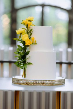 Bu göz kamaştırıcı çift katlı pasta pürüzsüz beyaz bir son içeriyor ve canlı sarı çiçekler ve yemyeşil ile güzelce süslenmiş, her kutlama için mükemmel..