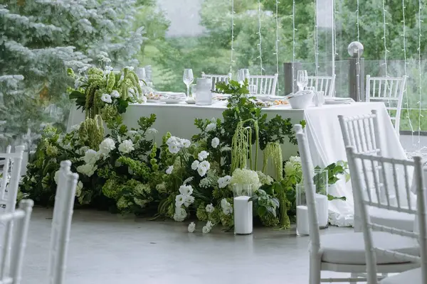 Güzel düzenlenmiş yeşil ve beyaz çiçekli bir masa zarif bir etkinlik için sakin bir atmosfer yaratır..