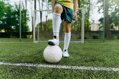Genç bir futbolcu, bir ayağı yemyeşil bir sahada topun üzerinde poz verir ve antrenman sırasında tekmeye hazırlanır..
