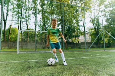 Genç bir çocuk, ağaçlarla çevrili bir alanda futbol yeteneklerini sergiliyor. Atletizm ve enerji gösterisi yapıyor..