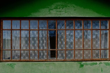 Yıpranmış ahşap çerçeveleri ve dantel perdeleri olan kırsal bir pencere, canlı yeşil bir duvara yaslanmış, huzurlu bir iç görünüm sergiliyor..