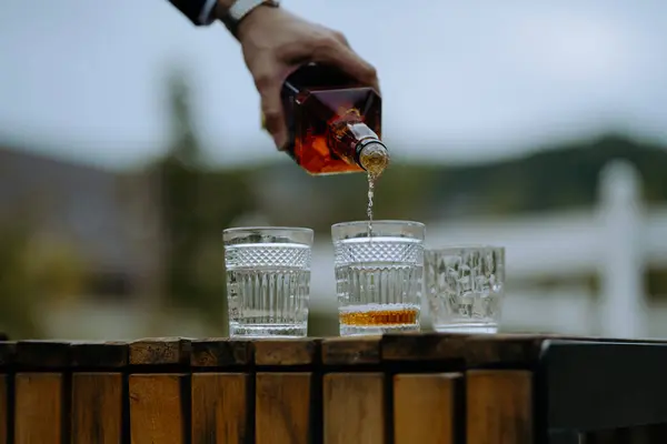 Bir el, açık hava etkinliği sırasında kristal bardaklara zengin bir içki doldurur. Mükemmel bir sofistike ve zevk anı yakalar..