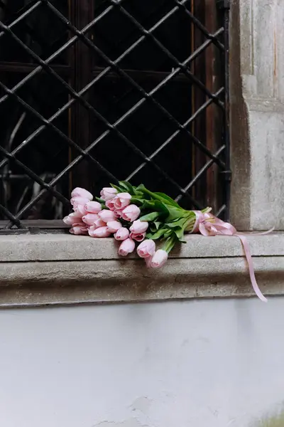 Yeşil yapraklı pembe lalelerin narin bir düzeni taş pencere pervazında uzanır. Klasik bir arka plana karşı güzellik ve zarafet sergilerler..