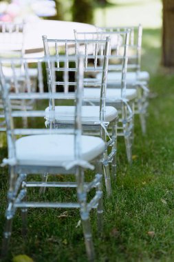 Açık hava kutlaması için beyaz yastıklı temiz plastik sandalyeler. Düğün ya da toplanma için mükemmel. Huzurlu bahçe atmosferiyle çevrili..