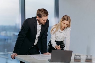 Profesyonel bir ikili modern bir ofiste planlarını inceler, modern bir ortamda işbirliği ve verimlilik gösterirler..