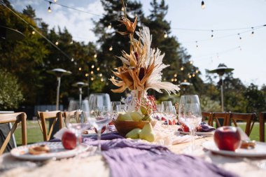 Güz süslemeleri, taze meyveler ve parlayan ışıklarla süslenmiş güzel bir açık hava yemek masası. Mevsimsel toplantılar ve kutlamalar için mükemmel..