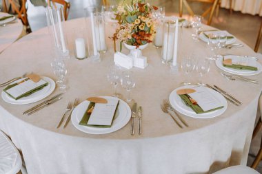 Güzelce düzenlenmiş yemek masasında zarif tabaklar, cam eşyalar, gümüş eşyalar ve davetliler için davetkar bir ortam yaratacak bir süs eşyası bulunuyor..