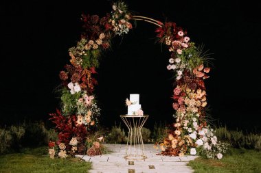 Güzel dekore edilmiş, canlı çiçeklerle dolu bir düğün kemeri ve şık beyaz bir pasta. Romantik bir akşam kutlaması için mükemmel hazırlanmış..