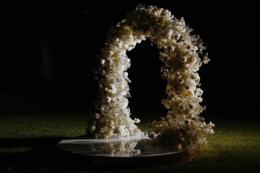 Göz kamaştırıcı bir çiçek kemeri, akşam ışığında güzelce aydınlatılmış, sakin bir dış mekanı süsler ve her olay için büyülü bir ortam yaratır..
