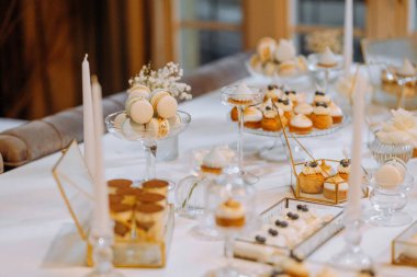 Çok güzel düzenlenmiş bir tatlı masasında bir dizi makaron, kek ve lezzetli pastalar sergileniyor. Kutlamalar için mükemmel bir ortam..