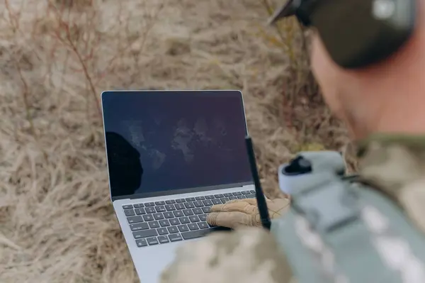 Taktik teçhizatlı bir asker, doğal arazi ile çevriliyken bir dizüstü bilgisayarla uğraşır ve askeri uygulamalardaki teknolojiyi vurgular..