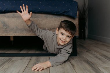 Neşeli bir çocuk neşeyle yatağın altından dışarı bakar, neşeyle el sallar, masum bir eğlence anı yaratır..