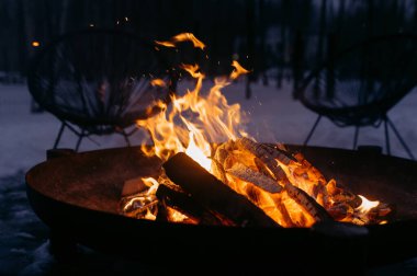 A warm, inviting bonfire in a fire pit surrounded by snowy scenery, creating a cozy atmosphere for winter gatherings and relaxation.