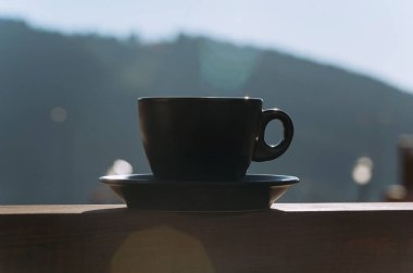 Bulanık bir dağ zemininde siyah bir kahve fincanının dinlendiği sakin bir sabah ayarı rahatlamanın özünü yakalıyor..