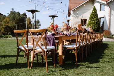Renkli çiçek süslemeleri, zarif sofra takımı ve rahat ışıklandırma içeren güzel bir açık hava yemek masası..