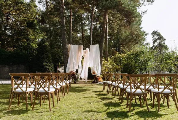 Ahşap sandalyeli, çiçekli süslemeli ve gür ormandaki katıksız perdeli güzel düzenlenmiş bir düğün sahnesi..