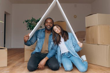 Neşeli bir çift yeni evlerinin keyfini çıkararak, paketlenmemiş karton kutular ve kapalı alandaki bitkilerin arasında rahat bir atmosfer yaratıyor..