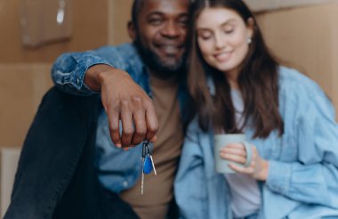 Yeni evlerinin anahtarlarını sergileyen mutlu bir çift sıcak bir ortamda kahvenin tadını çıkarırken yeni başlangıçları ve paylaşılan anları simgeliyor..