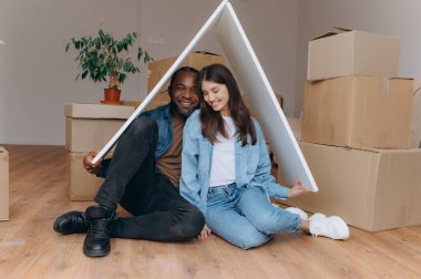 Neşeli bir çift yeni evlerinin keyfini çıkararak, paketlenmemiş karton kutular ve kapalı alandaki bitkilerin arasında rahat bir atmosfer yaratıyor..