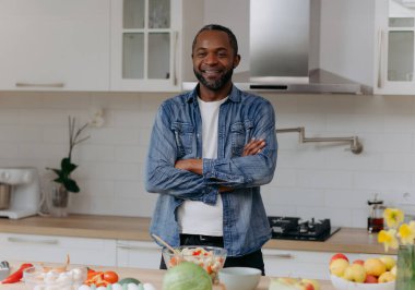 Kendine güvenen bir aşçı, modern bir mutfakta durup gülümseyerek taze malzemeler ve sebzelerle leziz yemekler yapmaya hazır, aşçılık tutkusu sergiliyor..