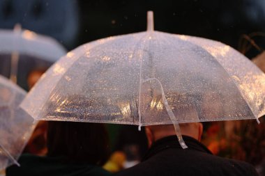 Yağmurlu bir akşamda şeffaf bir şemsiyeyi yakından görmek, samimi ve samimi bir atmosfer yaratır..
