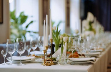 Zarif mumlar, laleler ve ince cam eşyalar içeren güzel düzenlenmiş bir yemek masası. Lüks bir toplantı ya da kutlama için mükemmel..