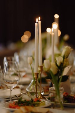 Yanan mumlar, taze beyaz çiçekler ve güzel hazırlanmış tabaklar içeren zarif bir yemek düzeni. Romantik ya da resmi bir toplantı için mükemmel..