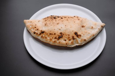 Taze pişmiş bir calzone, kıtır kıtır kıtır bir dokuya sahip, temiz beyaz tabakta servis edilen, yemek tutkunları ve mutfak vitrinleri için ideal..