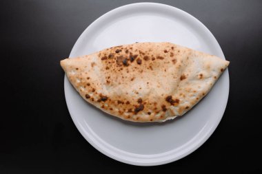 Lezzetli bir calzone beyaz bir tabakta oturup altın-kahverengi kabuğunu sergiliyor. Hızlı bir yemek veya atıştırmalık için mükemmel..