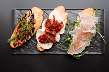 İçinde mozzarella, güneşte kurutulmuş domates, roka ve prosciutto bulunan nefis bir bruschetta gösterisi..