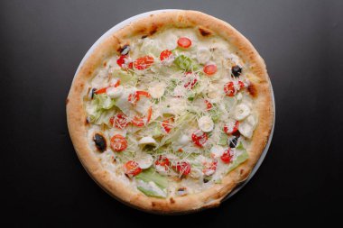 Koyu bir arka planda servis edilen canlı domates, marul ve zeytinli aromalı lezzetli bir pizza..