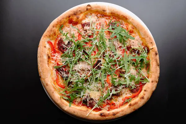 Ağız sulandıran bir gurme pizza. Üstünde roka, renkli biber ve tuzlu domates var. Pizzacılar için mükemmel..