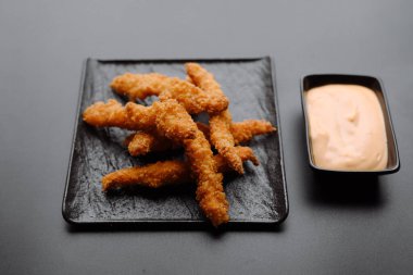 Baharatlı siyah bir tabakta sunulan çıtır tavuklar yanında sos ile lezzeti arttırır..