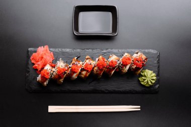 Kırmızı havyarla kaplanmış güzel suşi ruloları, siyah tahtada wasabi ve zencefil ile servis ediliyor, yemek severler için mükemmel..