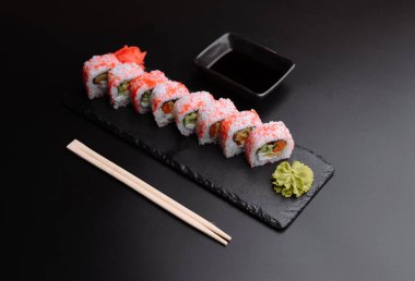 Renkli malzemelerle süslenmiş lezzetli suşi dürümleri, yanında wasabi ve soya sosu ile koyu bir tabakta servis edilir..