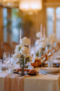 Beyaz güller, zarif cam eşyalar ve yumuşak mum ışığı olan güzel bir yemek masası özel durumlar için sıcak ve davetkar bir ortam yaratıyor..