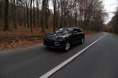 Siyah bir SUV, sakin bir ormanda sonbahar yapraklarıyla çevrili güzel bir yolda geziniyor..