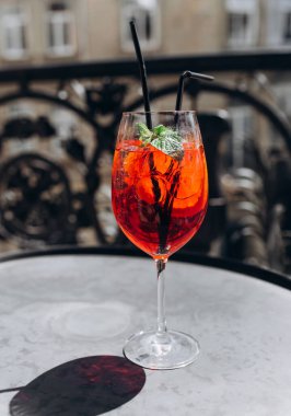 Nane yapraklarıyla süslenmiş canlı kırmızı bir kokteyl masanın üzerinde duruyor ve yaz rahatlığının esansını yakalıyor..