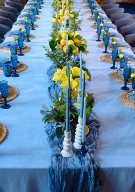 Taze limonlar, canlı sarı çiçekler ve mavi cam eşyalar içeren güzel bir masa. İlkbahar etkinlikleri için mükemmel..