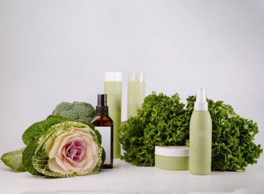 Doğal güzellik için taze marul, brokoli ve lahanayla çevrili organik cilt bakımı şişeleri ve kavanozlar..