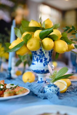 Mavi porselen vazoda yeşil yapraklı taze limonlar zarif bir masa süsü oluşturur..