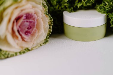 Süslü lahana yanında beyaz kapaklı yeşil kozmetik kavanozu. Organik cilt kavramları için mükemmel..