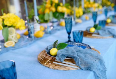 Güzel düzenlenmiş mavi ve sarı masa, limonlar, çiçekler ve yaz toplantıları için zarif cam eşyalar..