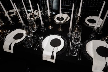 Resmi bir etkinlik için mumlar, cam eşyalar ve peçetelerle süslü lüks siyah beyaz masa..
